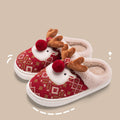 Women’s 3D reindeer Christmas plush slippers shown from an angled side product view, featuring a red and green holiday-patterned upper, dimensional reindeer face, brown antlers, red pom-pom nose, soft beige lining, and rounded open-back slipper silhouette.