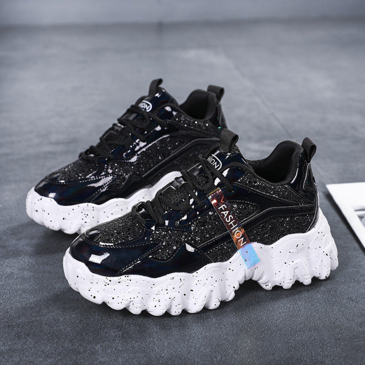 Pair of women's Nova Sparkle Luxe Chunky Sneakers in Black featuring dark layered uppers, subtle glossy and sparkle accents, black lace-up closures, rounded toes, and contrasting chunky white sculpted soles for bold Fall and Winter street-style outfits.