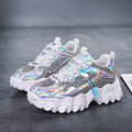 Pair of women's Nova Sparkle Luxe Chunky Sneakers in Silver with reflective iridescent detailing, light-colored lace-up uppers, shimmering multicolor accents, rounded athletic toes, and thick sculpted white soles for futuristic fashion-forward styling.