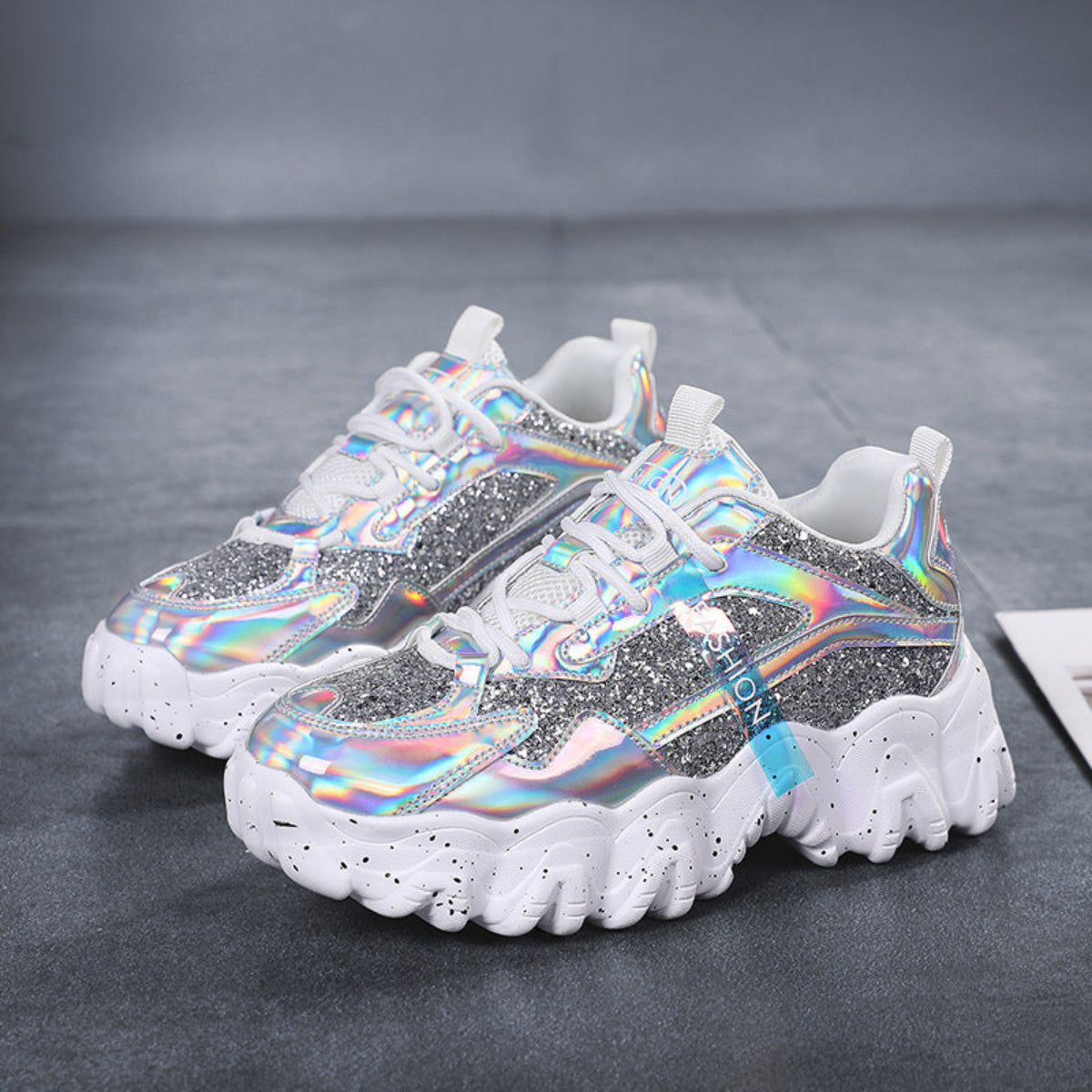 Pair of women's Nova Sparkle Luxe Chunky Sneakers in Silver with reflective iridescent detailing, light-colored lace-up uppers, shimmering multicolor accents, rounded athletic toes, and thick sculpted white soles for futuristic fashion-forward styling.