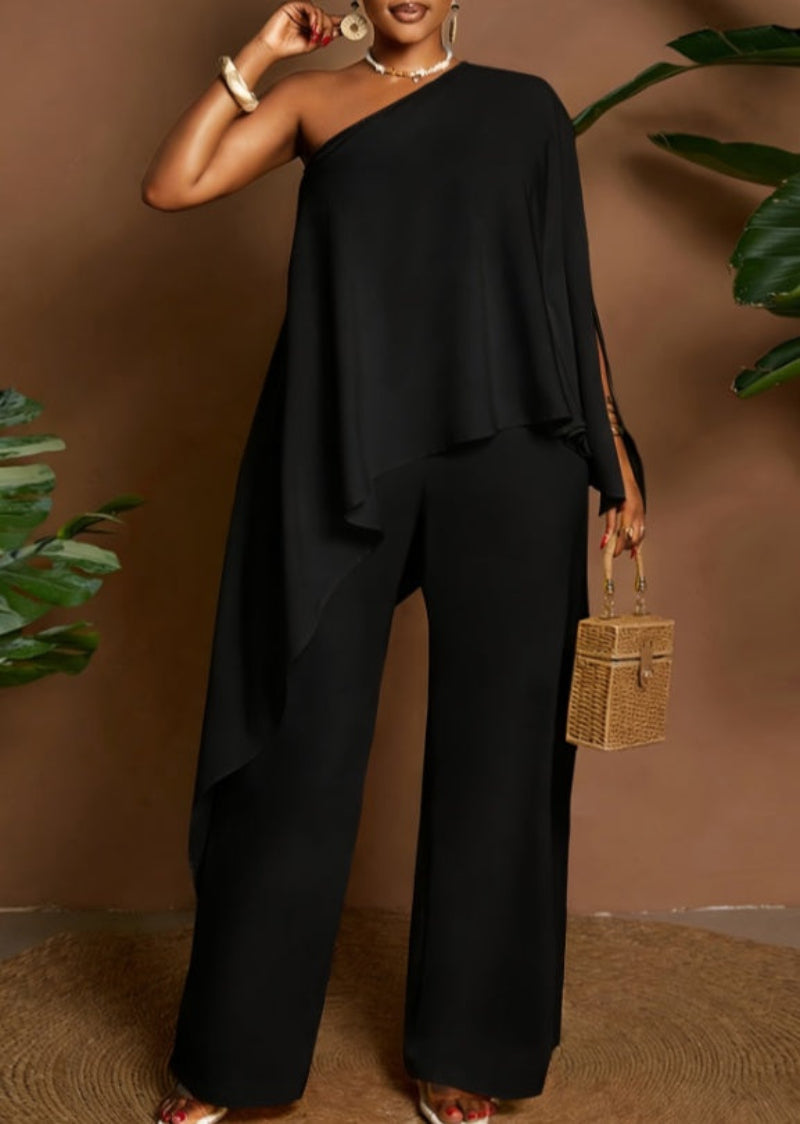Amara women's elegant black two-piece pants set shown from the front, featuring an asymmetrical one-shoulder top with a flowing cape-style overlay, draped fabric across the torso, and coordinating solid black wide-leg trousers.
