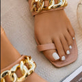 Apricot women’s flat slide sandals featuring a soft nude-toned upper strap, oversized shiny gold-tone chain detail across the front, open-toe design, and flat slip-on silhouette, shown worn on the foot from above to display the neutral color, comfortable fit, and elegant gold hardware.