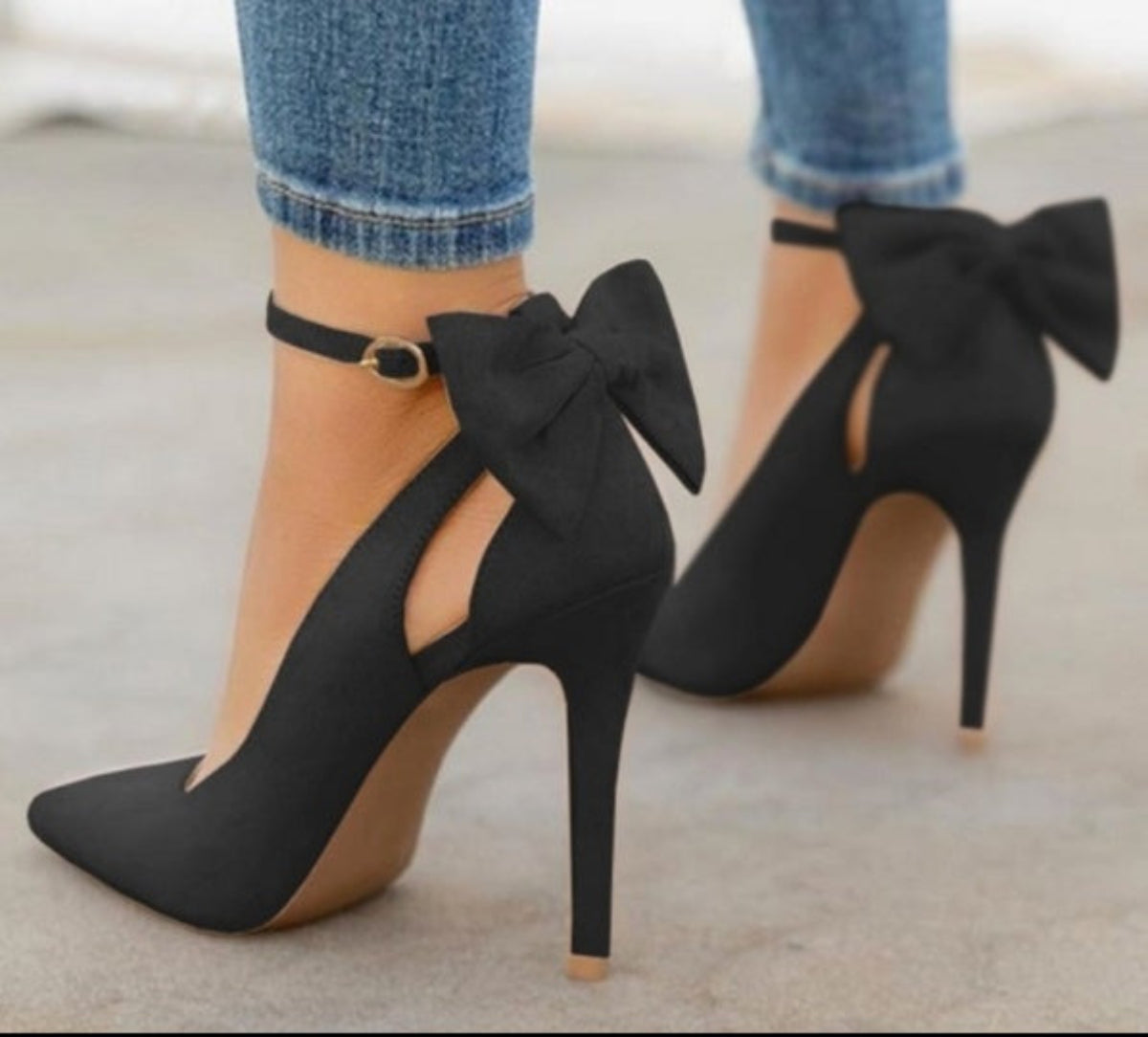 Black Arielle Bow Ankle-Strap Stiletto Pumps worn with cropped jeans, featuring large sculpted ankle bows, sleek pointed toes, slim stiletto heels, and an elegant all-black finish.