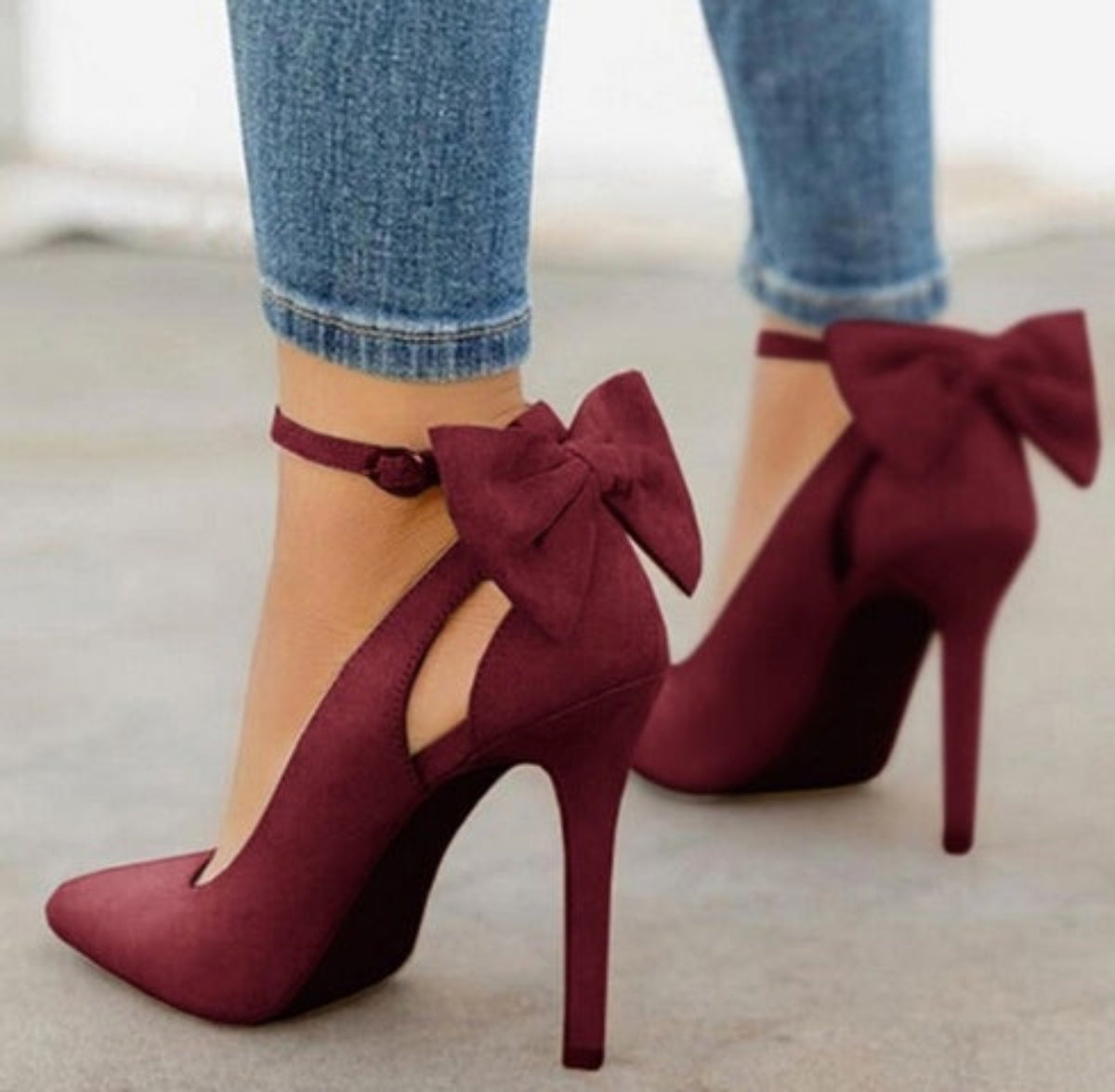 Dark Red Arielle Bow Ankle-Strap Stiletto Pumps worn with cropped denim, featuring oversized deep red ankle bows, pointed toes, and slim stiletto heels for a rich Fall and Winter statement look.