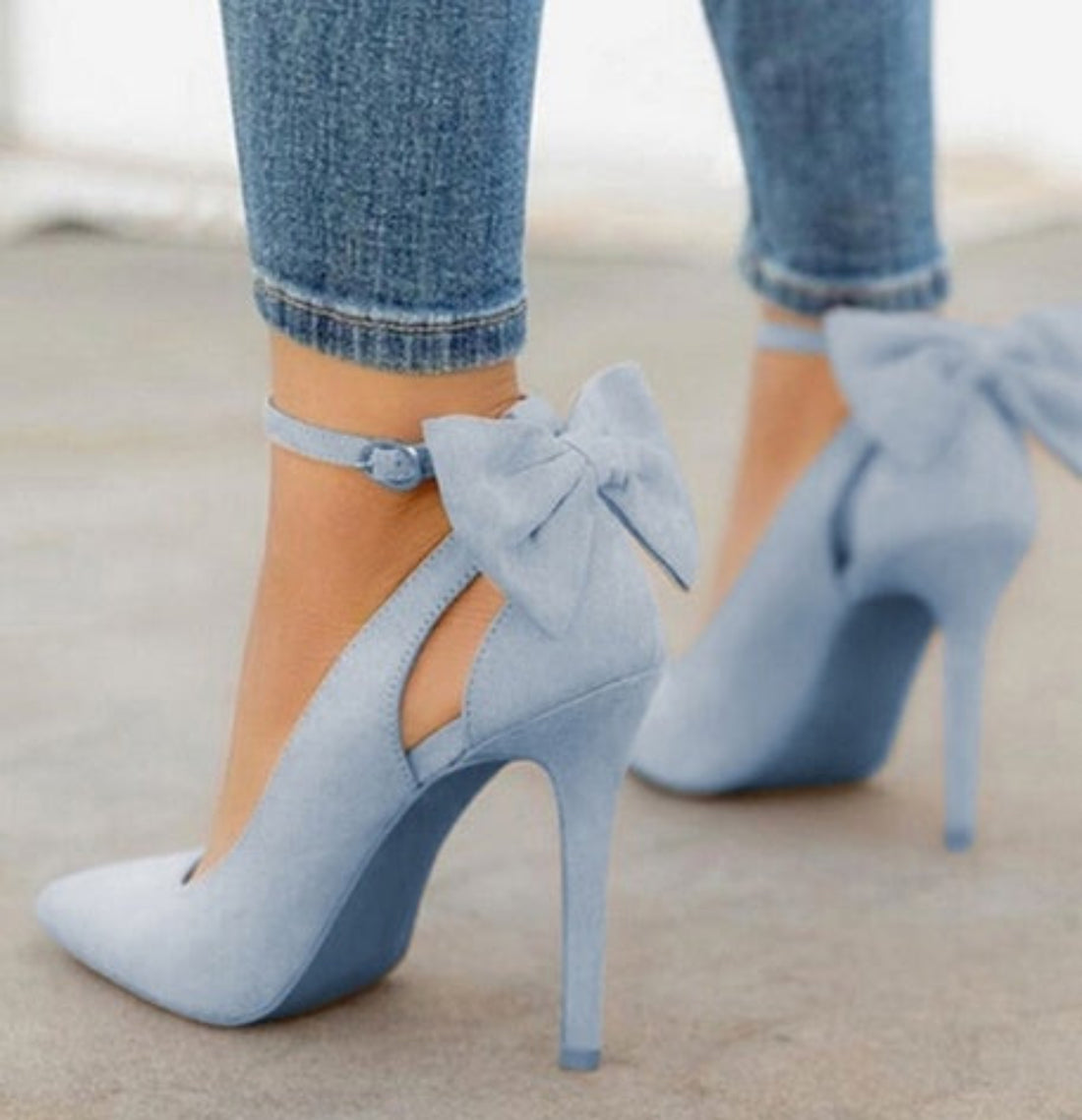 Light Blue Jean Arielle Bow Ankle-Strap Stiletto Pumps worn with cropped denim, featuring oversized statement bows at the ankle, soft blue fabric texture, pointed toes, and slim high stiletto heels.
