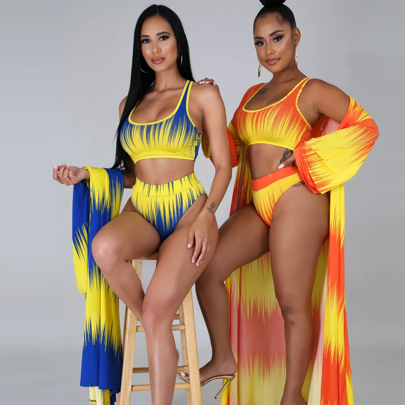 Side-by-side view of two models wearing the Azaria Sunset resort swimwear set in blue-and-yellow and orange-and-yellow combinations, showing the matching cropped swim tops, high-waisted bottoms, and coordinating long flowing cover-ups.
