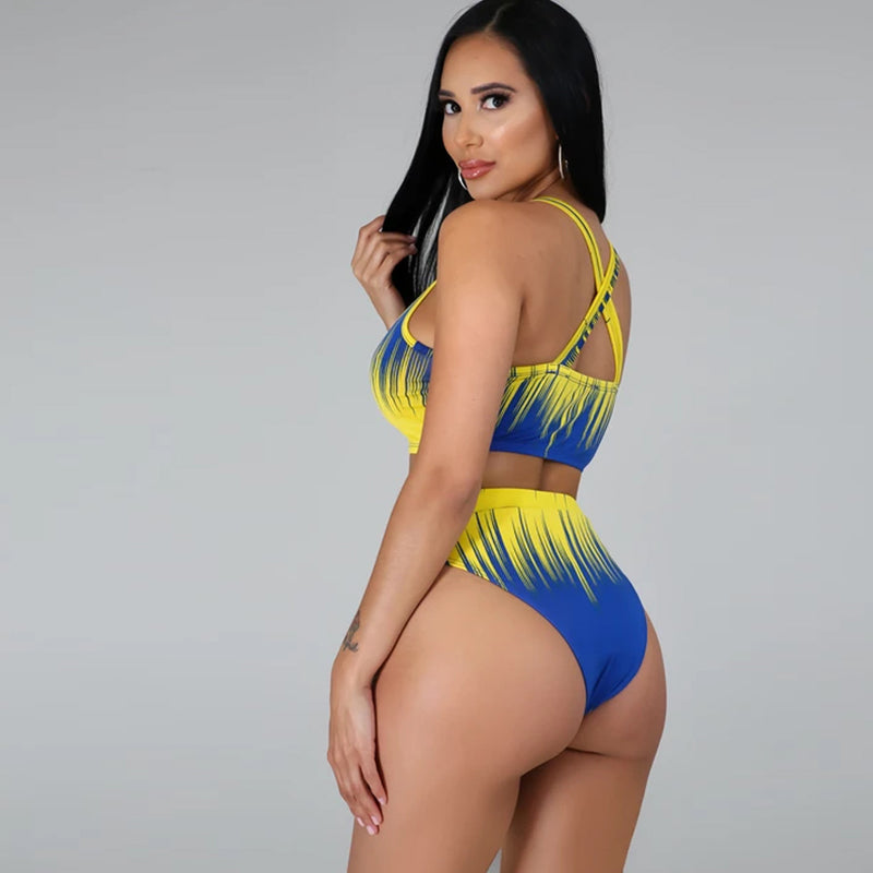 Side-by-side view of two models wearing the Azaria Sunset resort swimwear set in blue-and-yellow and orange-and-yellow combinations, showing the matching cropped swim tops, high-waisted bottoms, and coordinating long flowing cover-ups.