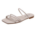 Beige women’s minimalist flat sandals featuring delicate slim straps across the toes and forefoot, a modern open square-toe silhouette, matching neutral footbed, and low flat sole, shown from an angled three-quarter product view on a white background.
