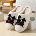 Cream women’s plush Halloween slippers featuring bold black and orange seasonal artwork across the front, soft fuzzy closed-toe construction, plush lining, and rounded slip-on silhouette, displayed together as a matching pair to highlight the dark Halloween design against the light cream background.