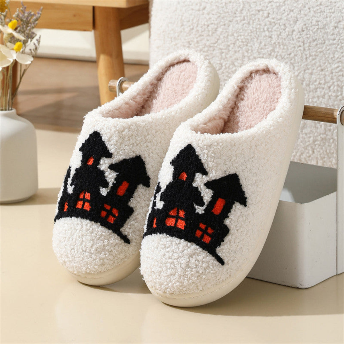 Cream women’s plush Halloween slippers featuring bold black and orange seasonal artwork across the front, soft fuzzy closed-toe construction, plush lining, and rounded slip-on silhouette, displayed together as a matching pair to highlight the dark Halloween design against the light cream background.