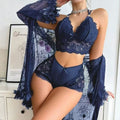 Front view of a woman modeling the Brielle dark blue three-piece lingerie ensemble, featuring a dark blue lace top with decorative cutout styling, coordinating high-waisted dark blue bottoms, and a flowing sheer navy cover-up with wide long sleeves.