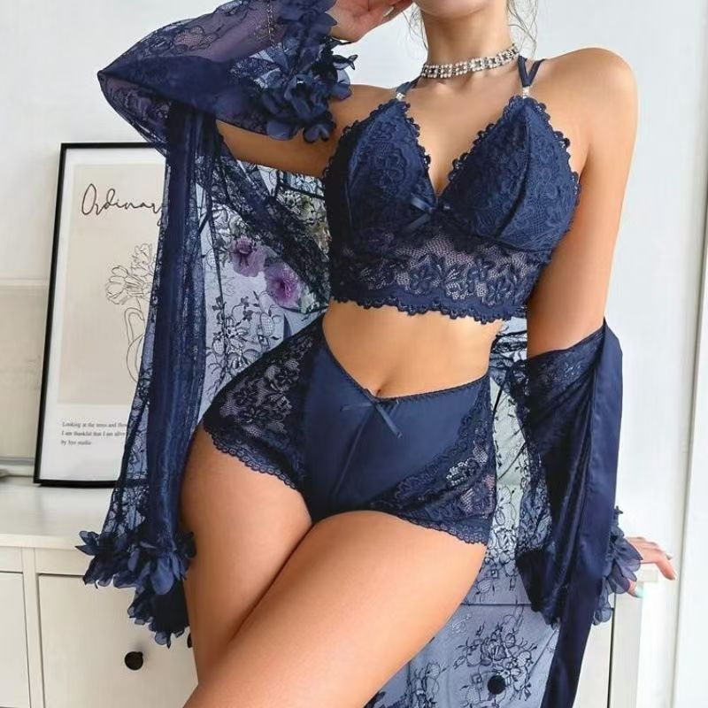 Front view of a woman modeling the Brielle dark blue three-piece lingerie ensemble, featuring a dark blue lace top with decorative cutout styling, coordinating high-waisted dark blue bottoms, and a flowing sheer navy cover-up with wide long sleeves.