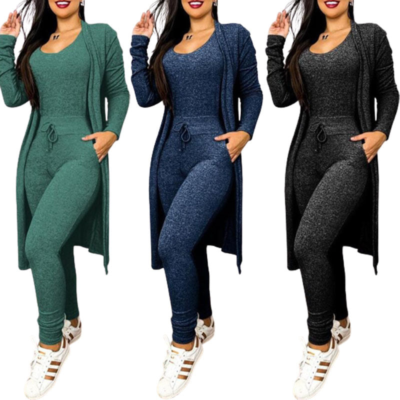 Brielle women's cozy knit-look jumpsuit and long cardigan sets displayed side by side in green, navy blue, and charcoal black, featuring fitted sleeveless scoop-neck jumpsuits with adjustable drawstring waists, tapered pant legs, and matching long-sleeve open-front cardigans extending below the hips, styled with white casual sneakers.