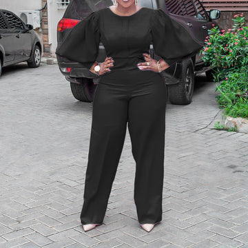 Detail view of the Cambria women's black jumpsuit focusing on the voluminous puff sleeve construction, smooth bodice, fitted waist shaping, and the clean transition into wide-leg trousers.