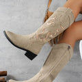 Woman wearing beige Camille pointed-toe riding boots while seated, highlighting the tall embroidered shafts, elegant pointed toes, Western-inspired detailing, and comfortable chunky heels.