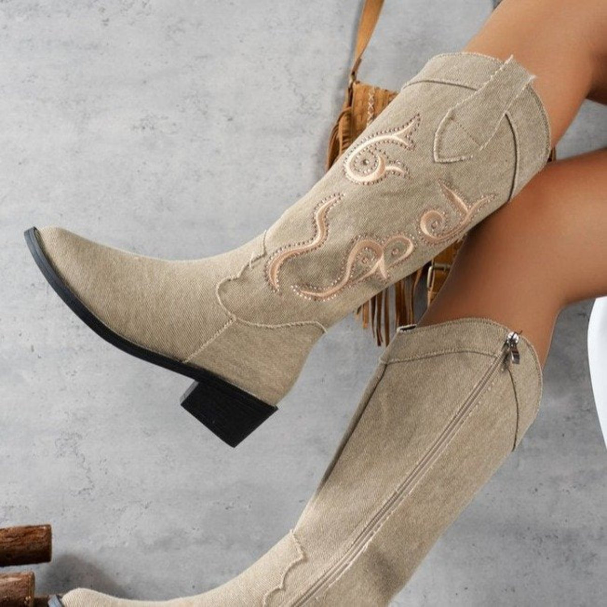 Woman wearing beige Camille pointed-toe riding boots while seated, highlighting the tall embroidered shafts, elegant pointed toes, Western-inspired detailing, and comfortable chunky heels.