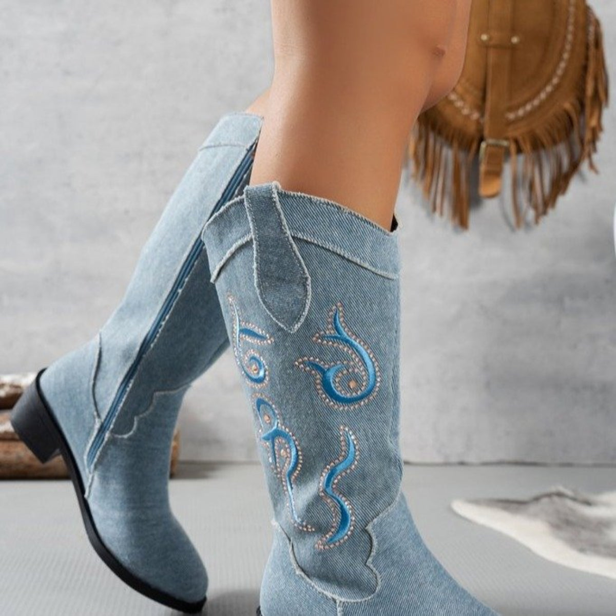 Side view of women’s light blue Camille tall riding boots showing the pointed toe, embroidered Western-style shaft detailing, curved boot opening, and stable chunky heel.