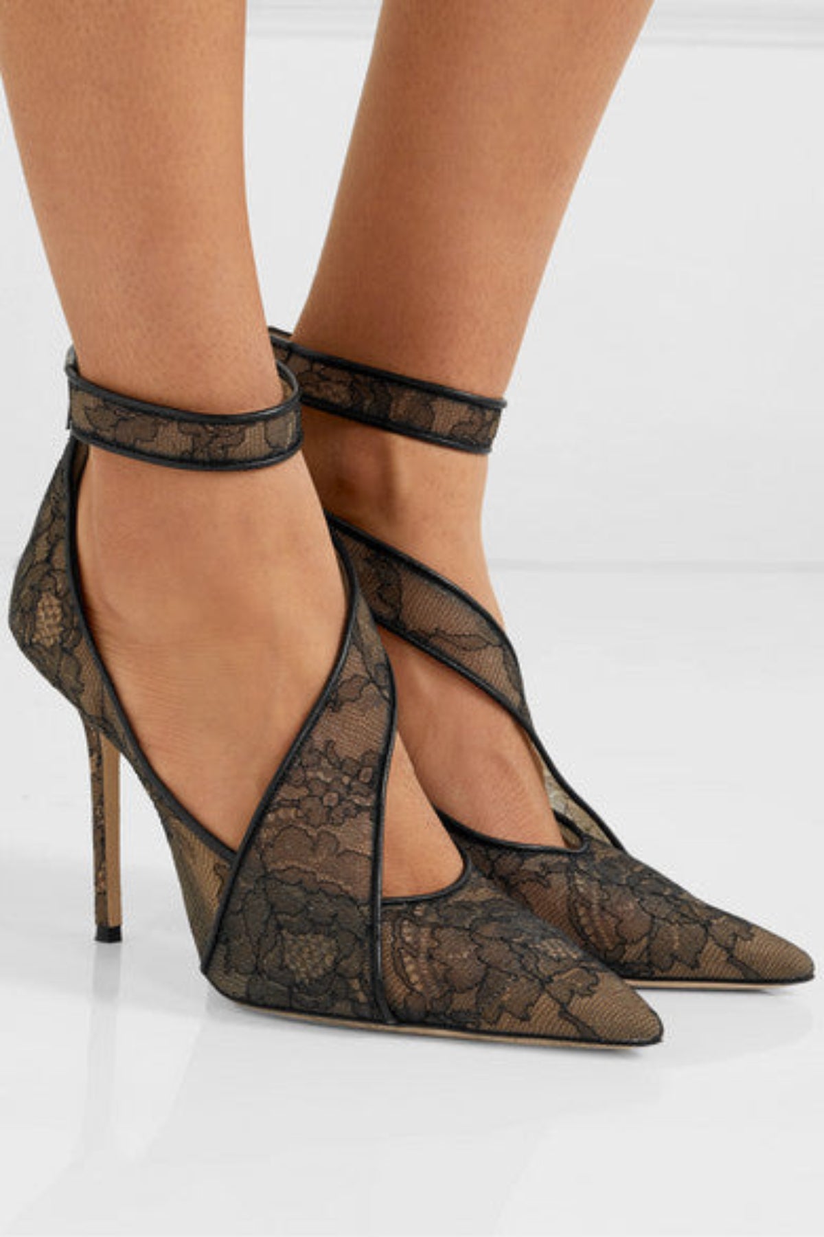 Black Celeste Lace Pointed-Toe Stiletto Pumps worn on a model, showing the semi-sheer lace design across the foot, pointed toes, secure ankle straps, and slender high heels.
