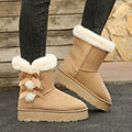 Woman wearing beige Cozy Belle fleece-lined ankle boots with dark pants, highlighting the plush white cuff, feminine bow accents, warm ankle-height construction, and chunky winter sole.