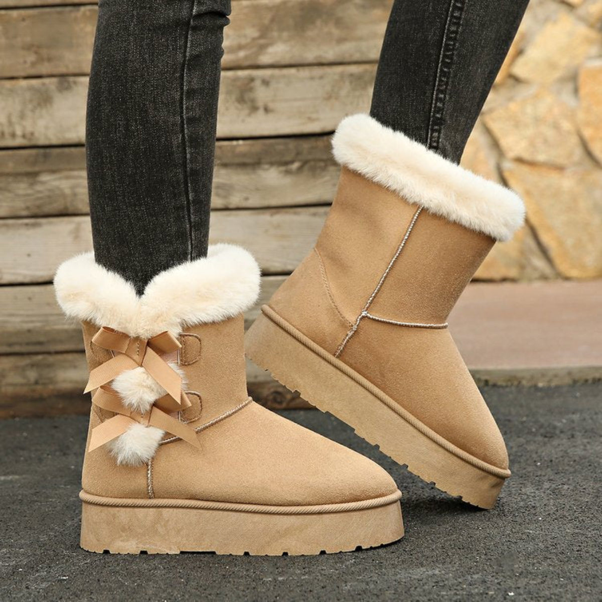 Woman wearing beige Cozy Belle fleece-lined ankle boots with dark pants, highlighting the plush white cuff, feminine bow accents, warm ankle-height construction, and chunky winter sole.