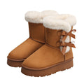 Women’s camel Cozy Belle fleece-lined ankle boots featuring plush white faux-fur cuffs, double decorative side bow accents, rounded toes, visible contrast stitching, soft suede-style uppers, and thick brown platform soles shown as a pair against a clean white background.