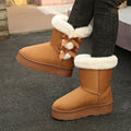 Women’s camel Cozy Belle fleece-lined ankle boots featuring soft white faux-fur trim, decorative brown bow accents, rounded toes, and thick textured soles designed for cozy everyday winter outfits.