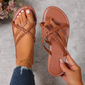 Dark brown women’s braided cross-strap toe-ring flat sandals with woven straps crossing over the foot, open-toe styling, coordinating brown flat footbed, and contrast stitching around the sole, shown with one sandal worn and the matching sandal held for a clear product view