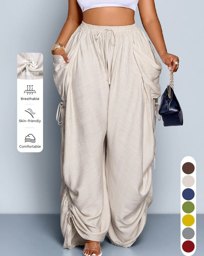 Delilah women's beige wide-leg pants shown on a model, featuring a gathered high-rise waistband with long drawstring ties, oversized cargo pockets at the sides, flowing lightweight-looking fabric, and ruched lower leg detailing for a relaxed oversized boutique fashion look.