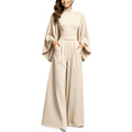 Eliana women's elegant apricot jumpsuit displayed from the front, featuring a high neckline, loose flowing cape-inspired sleeves, a defined waist, front pleated wide-leg trousers, and a sophisticated floor-length silhouette.
