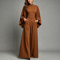 Eliana women's elegant caramel wide-leg jumpsuit shown from the front, featuring a fitted high-neck bodice, dramatic flowing cape-style long sleeves, a defined waistband, front pleated detailing, side pockets, and floor-length wide-leg trousers.