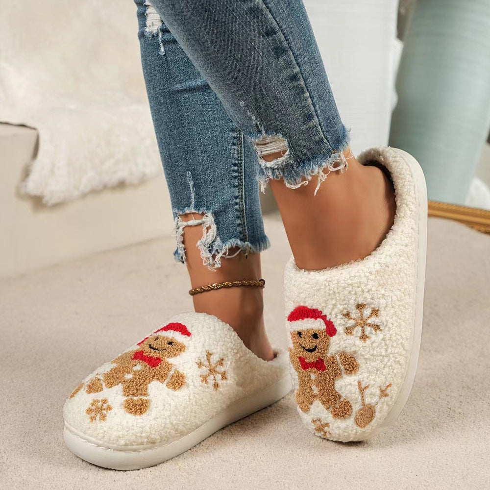 White women’s plush Christmas slippers featuring embroidered gingerbread characters wearing festive red holiday hats and scarves, brown snowflake accents, soft fuzzy closed-toe uppers, and cozy cream lining, displayed together from the front for a clear view of the gingerbread and winter-themed embroidery.