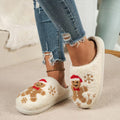 White gingerbread Christmas plush slippers for women shown worn with cropped blue jeans, featuring fuzzy closed-toe construction, embroidered brown gingerbread characters with red holiday accents, snowflake details, and soft cream plush lining for a festive winter look.