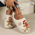 White women’s gingerbread holiday plush slippers shown in a close detail view, featuring textured fuzzy fabric, embroidered gingerbread characters with festive red accents, brown snowflake motifs, rounded closed toes, and soft cream lining for a cozy Christmas design.