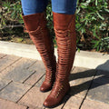 Woman wearing brown Harper cross-strap knee-high boots outdoors, featuring a tall fitted shaft, layered strap detailing, rounded toe, and comfortable block heel styled with blue jeans.