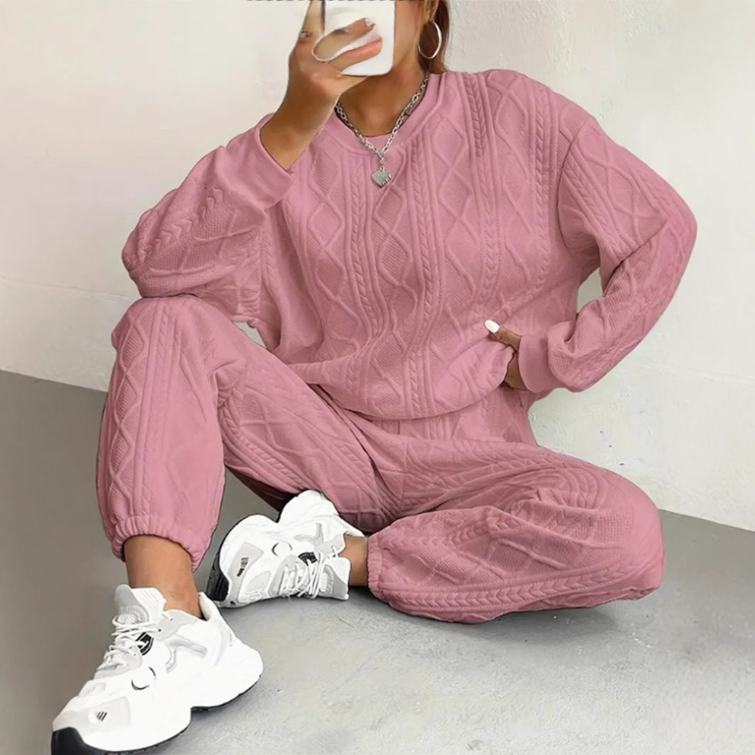 Harper women's dusty pink cable-knit matching lounge set shown on a seated model, featuring a relaxed long-sleeve crewneck sweater with raised textured knit patterns, matching drawstring jogger pants with tapered ankles, and chunky white athletic sneakers.