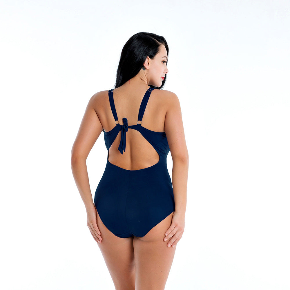 Rear view of a model wearing the Kendra navy-blue one-piece swimsuit, showing the wide shoulder straps, deep back opening, and smooth solid-color fabric extending across the lower back and hips.