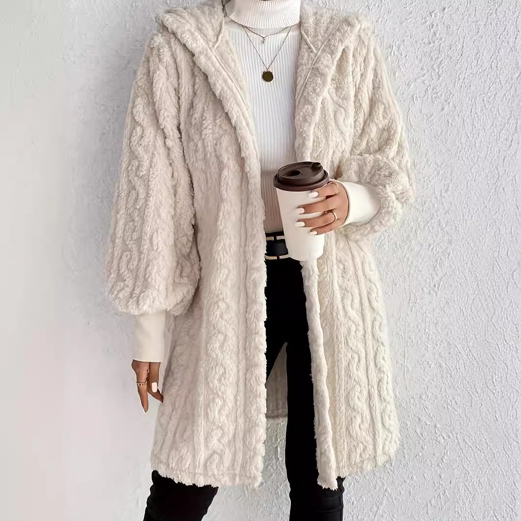 Woman wearing an white milk hooded teddy longline coat over a white turtleneck and black pants while holding a coffee cup against a light neutral wall.