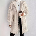 Woman wearing an white milk hooded teddy longline coat over a white turtleneck and black pants while holding a coffee cup against a light neutral wall.