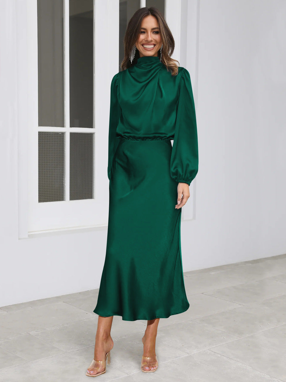 Emerald green draped satin maxi dress with long sleeves, high neckline, and flowing skirt.