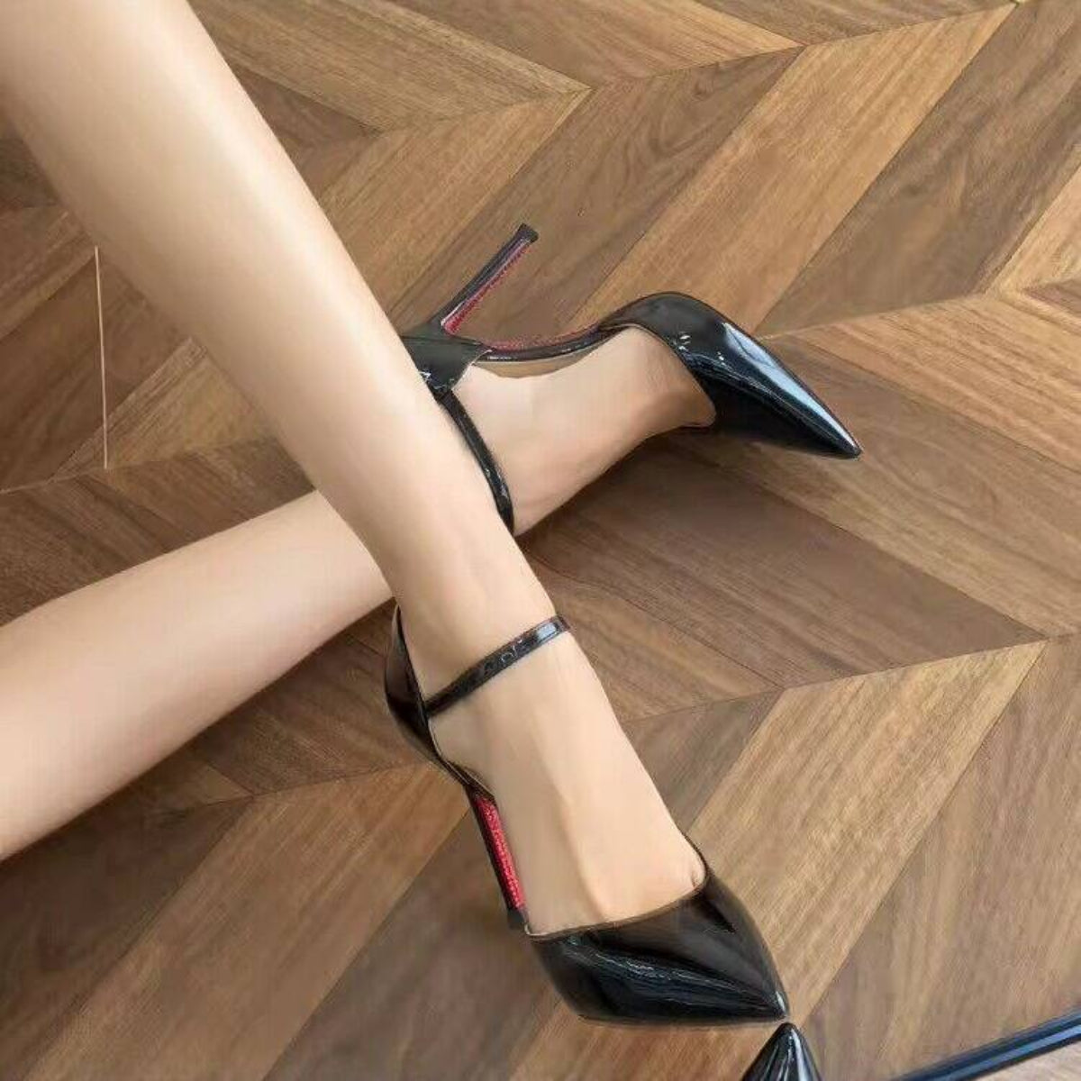 Black Monroe Pointed-Toe Slingback Pump worn from the side on a wood floor, featuring a glossy pointed toe, delicate ankle strap, slim stiletto heel, and polished evening-shoe appearance.