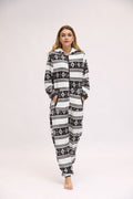 Full-length front view of the Noelle black and white hooded pajama onesie worn by a woman standing against a light studio background, featuring black reindeer silhouettes, white snowflake and winter-inspired geometric patterns, a front zipper, attached hood with drawstrings, and tapered full-length legs with gathered cuffs.