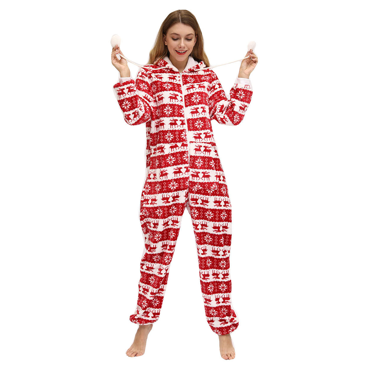 Full-length front view of the Noelle women's red and white Christmas pajama onesie worn by a female model, featuring alternating horizontal rows of red reindeer silhouettes, intricate snowflake motifs, and geometric Nordic-inspired patterns against a white background, with a front zipper closure, long sleeves, attached hood, and gathered ankle cuffs.