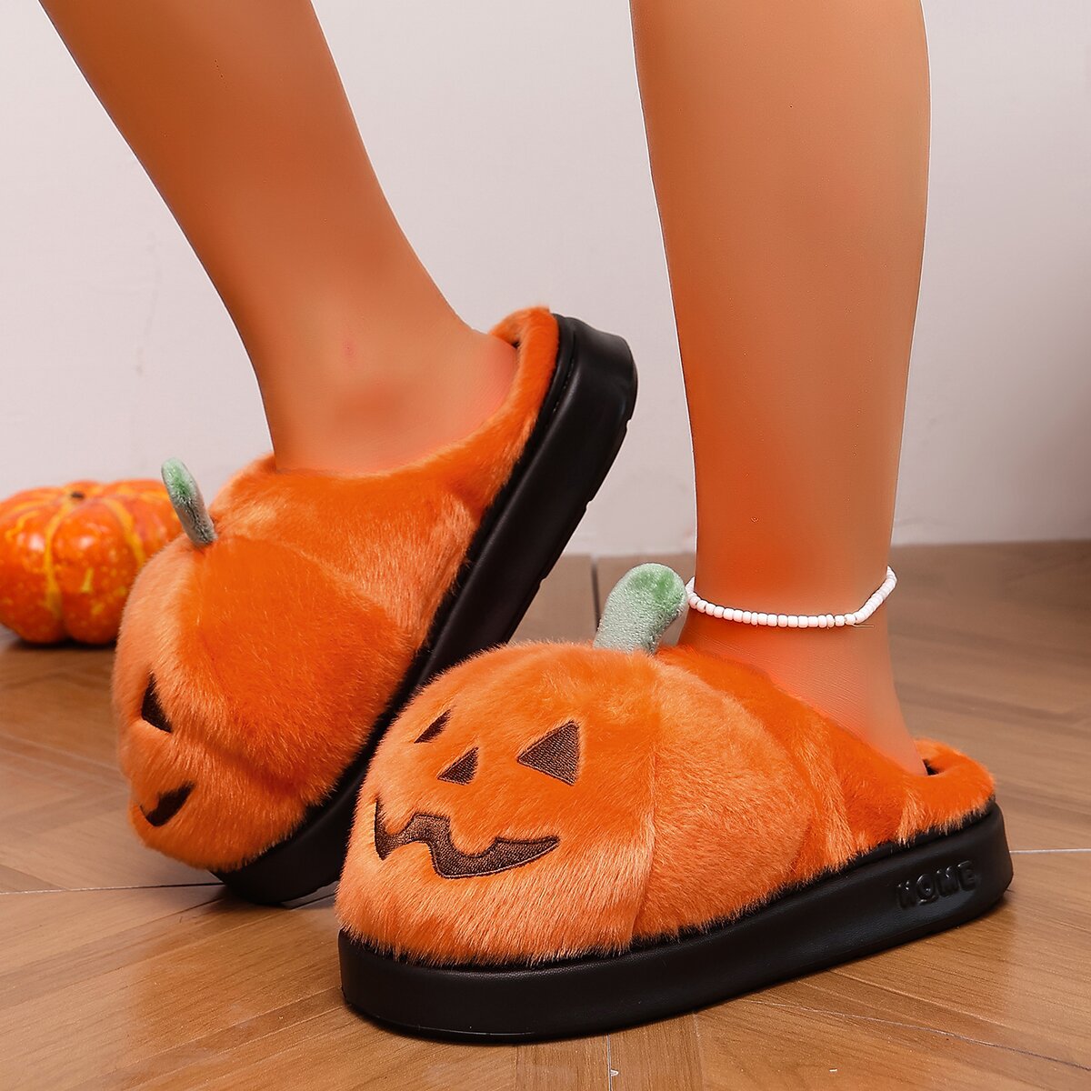 Orange women’s plush pumpkin Halloween slippers shown worn from an angled side view, featuring fuzzy pumpkin-shaped uppers with black jack-o’-lantern facial details, green stem accents, open-back construction, and thick black platform-style soles for cozy seasonal indoor wear.