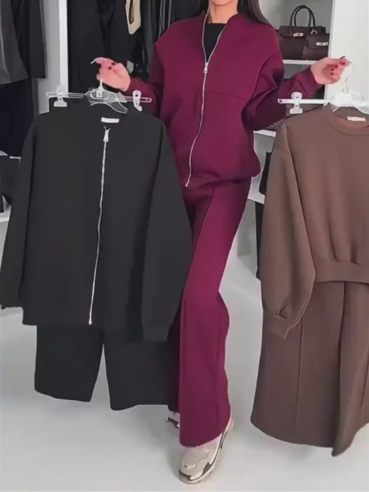 Model showcasing burgundy tracksuit while holding black and brown zip-up outfits on hangers