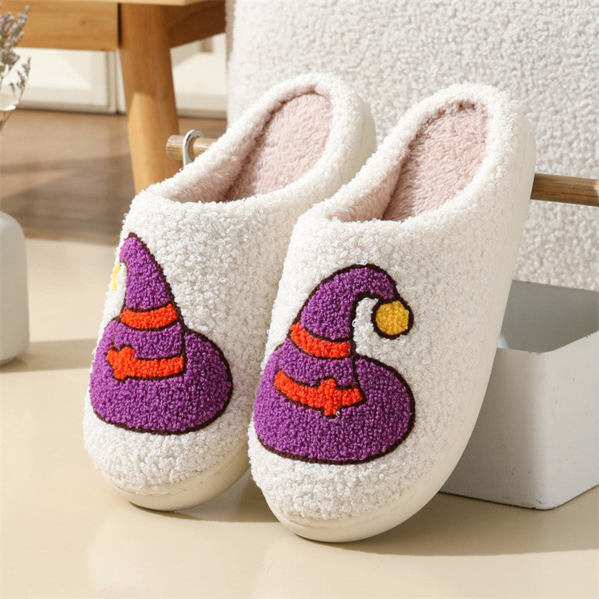 Cream women’s plush Halloween slippers featuring embroidered purple witch hats with orange bands and curved pointed tops, soft fuzzy closed-toe uppers, cozy lining, and an easy slip-on shape, displayed as a matching pair for a clear view of the colorful witch-themed artwork.