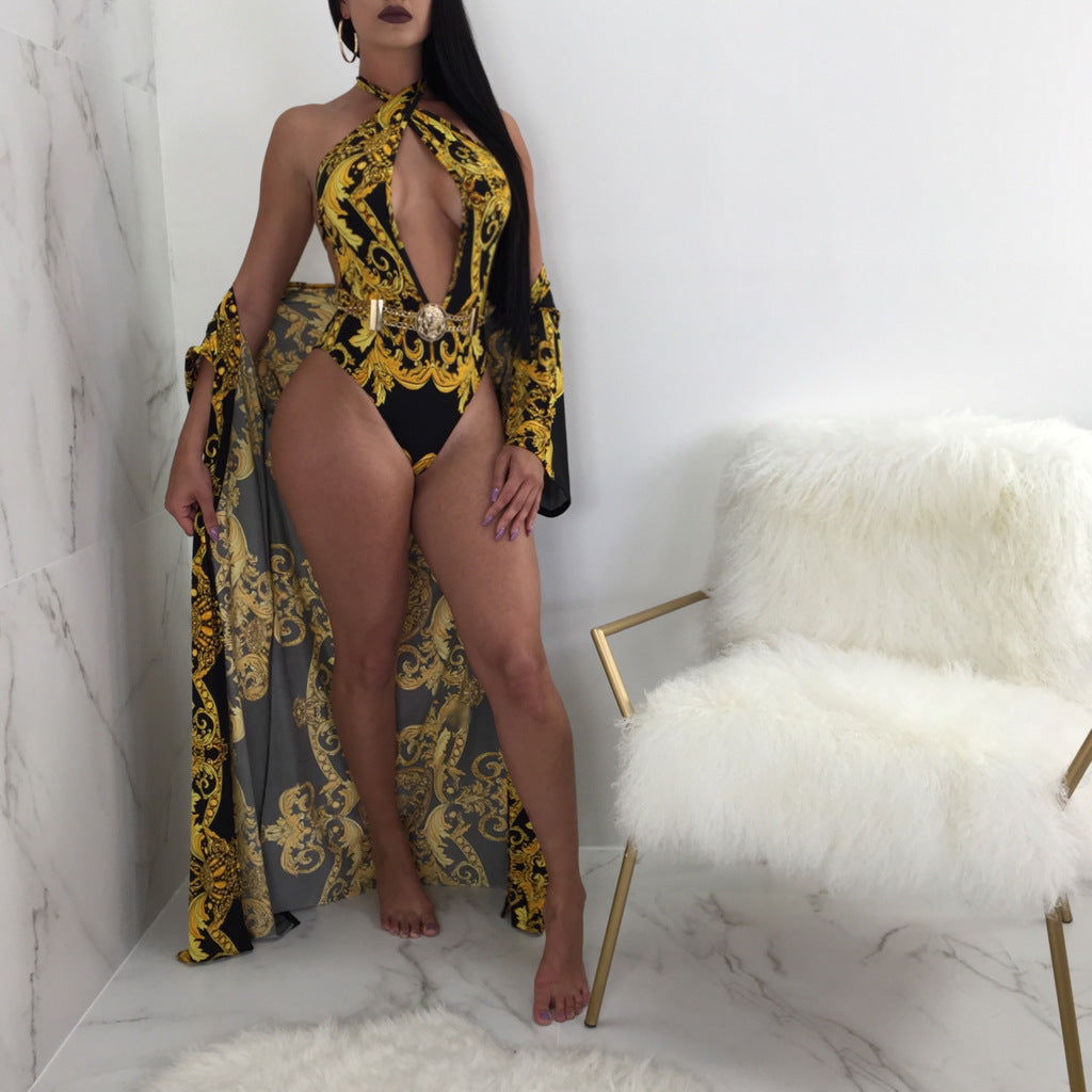 Safiya women's black-and-gold printed resort swimwear set shown on a model wearing a plunging black swimsuit decorated with elaborate gold baroque-style floral and scroll patterns, paired with a long matching open-front cover-up featuring coordinated black-and-gold ornamental designs.