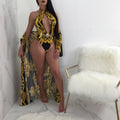 Front view of a model wearing the Safiya black-and-gold printed swimsuit featuring a high halter-style neckline, dramatic teardrop-shaped chest cutout, ornate gold scrolling patterns, and a coordinating flowing black-and-gold beach cover-up extending below the hips.