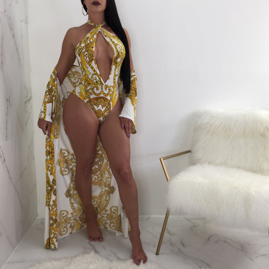 Front view of a model wearing the Safiya white-and-gold printed swimsuit featuring a high halter-style neckline, dramatic teardrop-shaped chest cutout, ornate gold scrolling patterns, and a coordinating flowing white-and-gold beach cover-up extending below the hips.