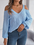 Woman wearing a light blue cold-shoulder V-neck textured knit sweater with blue jeans indoors.