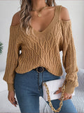 Woman wearing a khaki cable knit sweater and blue jeans, holding a purse with gold chain strap.